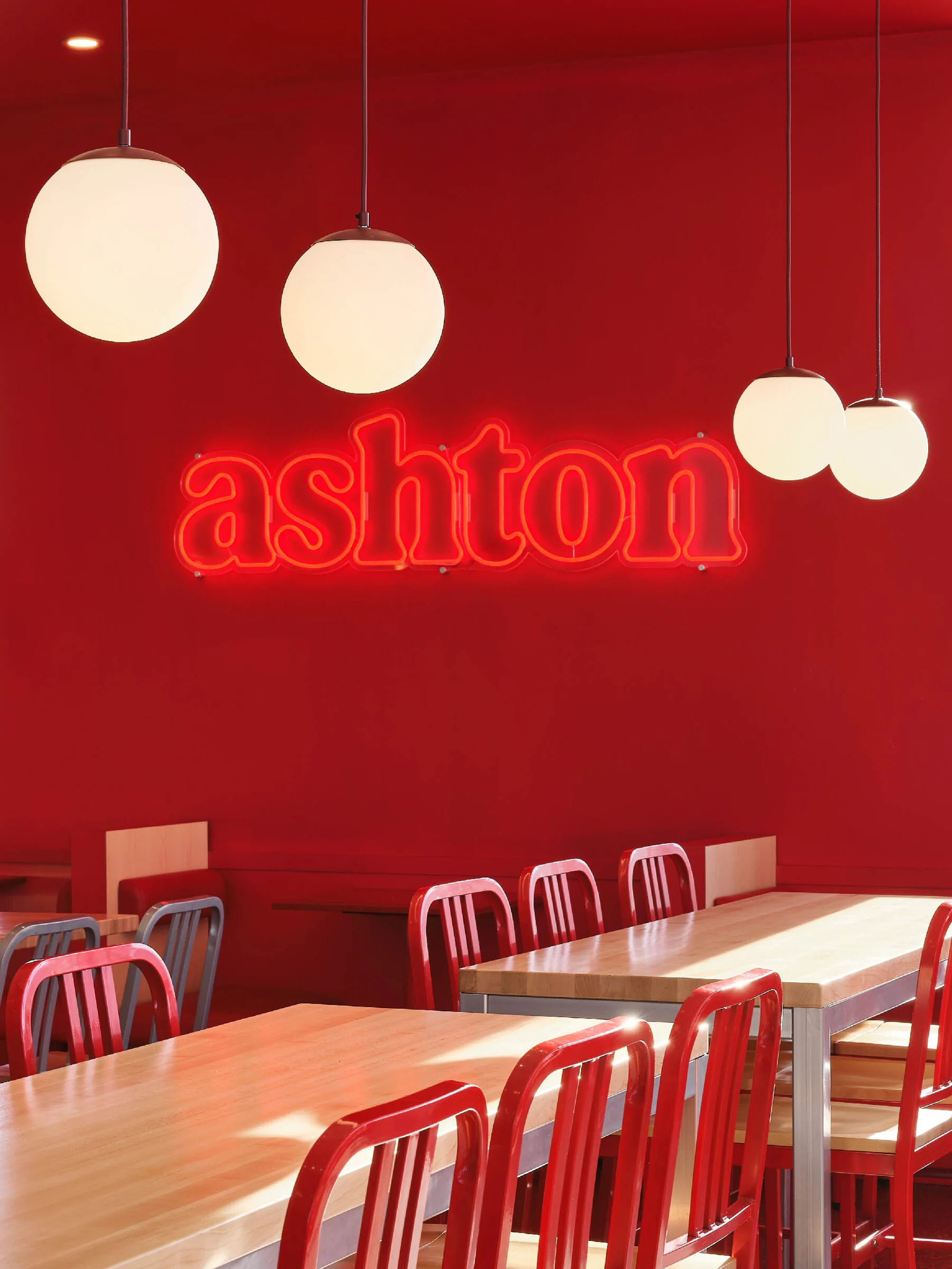Restaurant interior with red walls, wooden tables, and hanging spherical lights under a bright, inviting light.