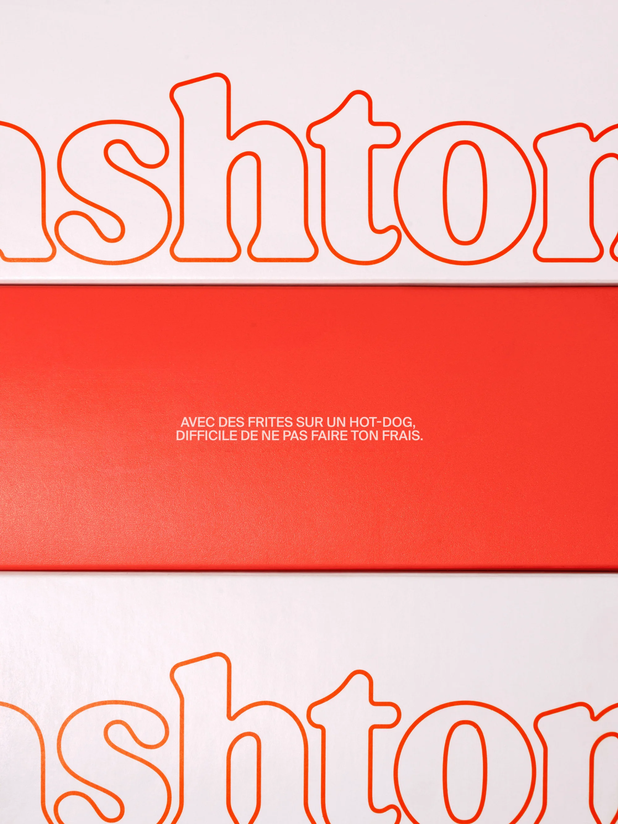 Abstract product shot featuring the name brand 'ashton' with a French tagline on a background of contrasting white and coral.