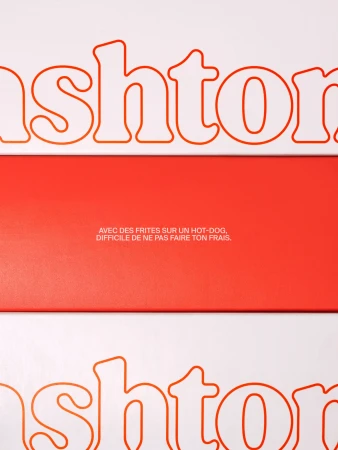 Abstract product shot featuring the name brand 'ashton' with a French tagline on a background of contrasting white and coral.