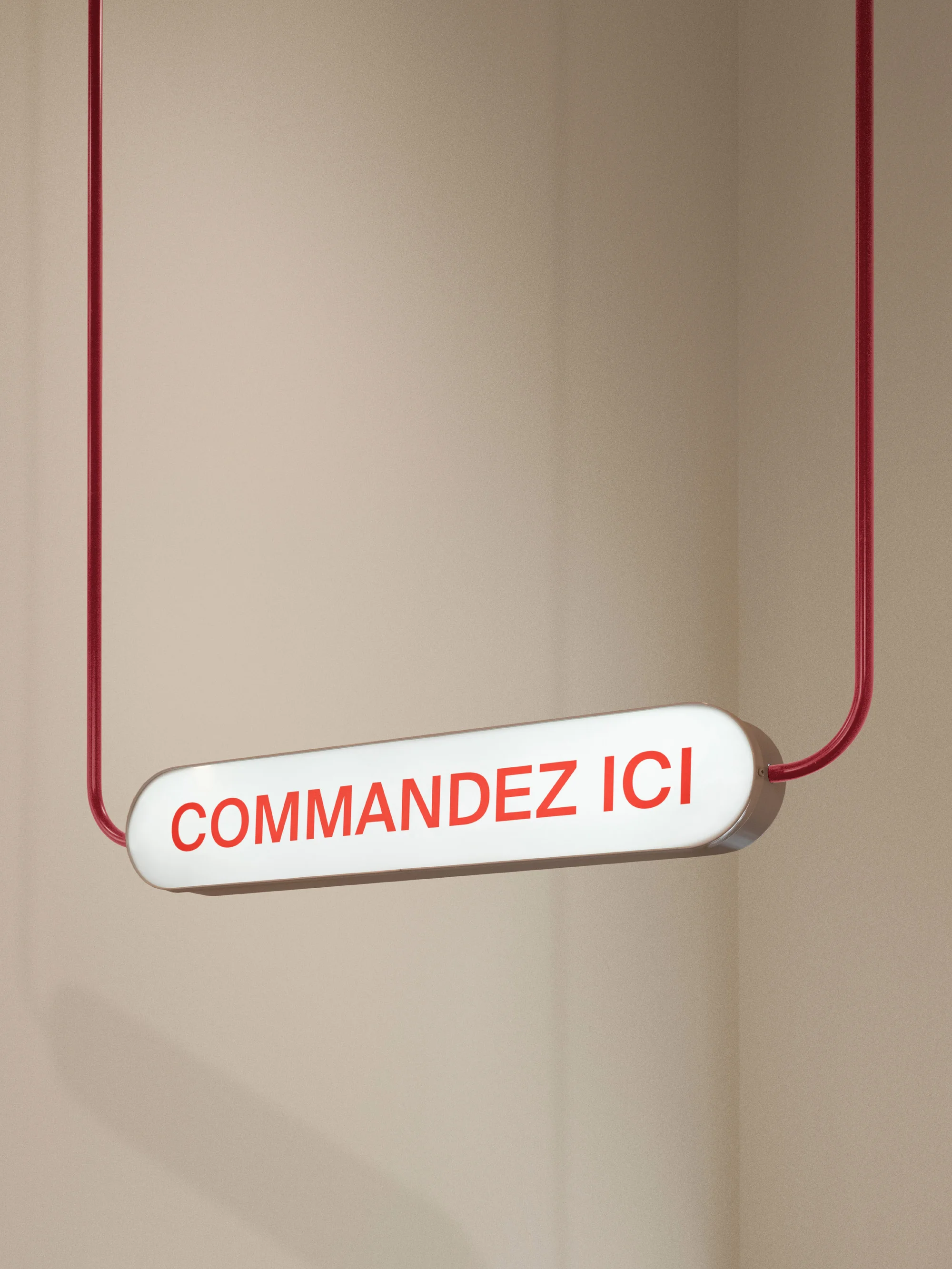 Illuminated sign suspended by red cables against a beige wall, displaying the French text "COMMANDEZ ICI" in red letters.