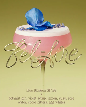 A pink cocktail in a stemmed glass is garnished with a blue flower and served on a yellow surface with cocktail ingredients.
