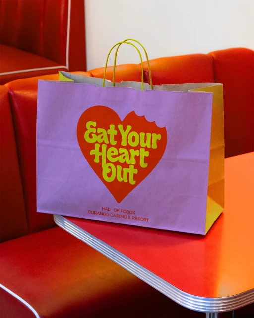 A gift bag from Durango Casino and Resort with a playful heart design sits on an orange diner booth seat against a white background.