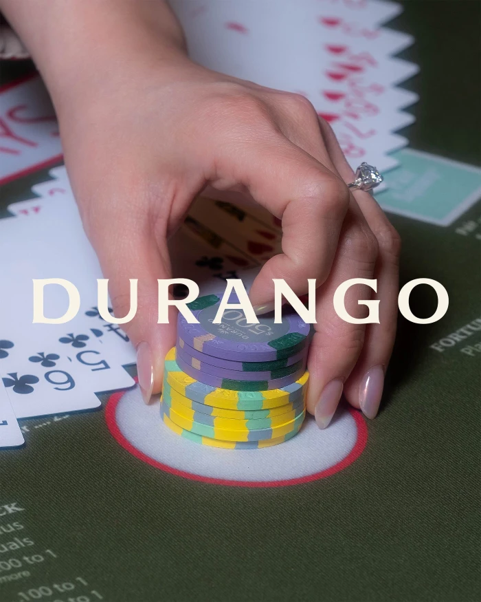 Close-up of a person's hand stacking colourful casino chips on a green felt table with playing cards