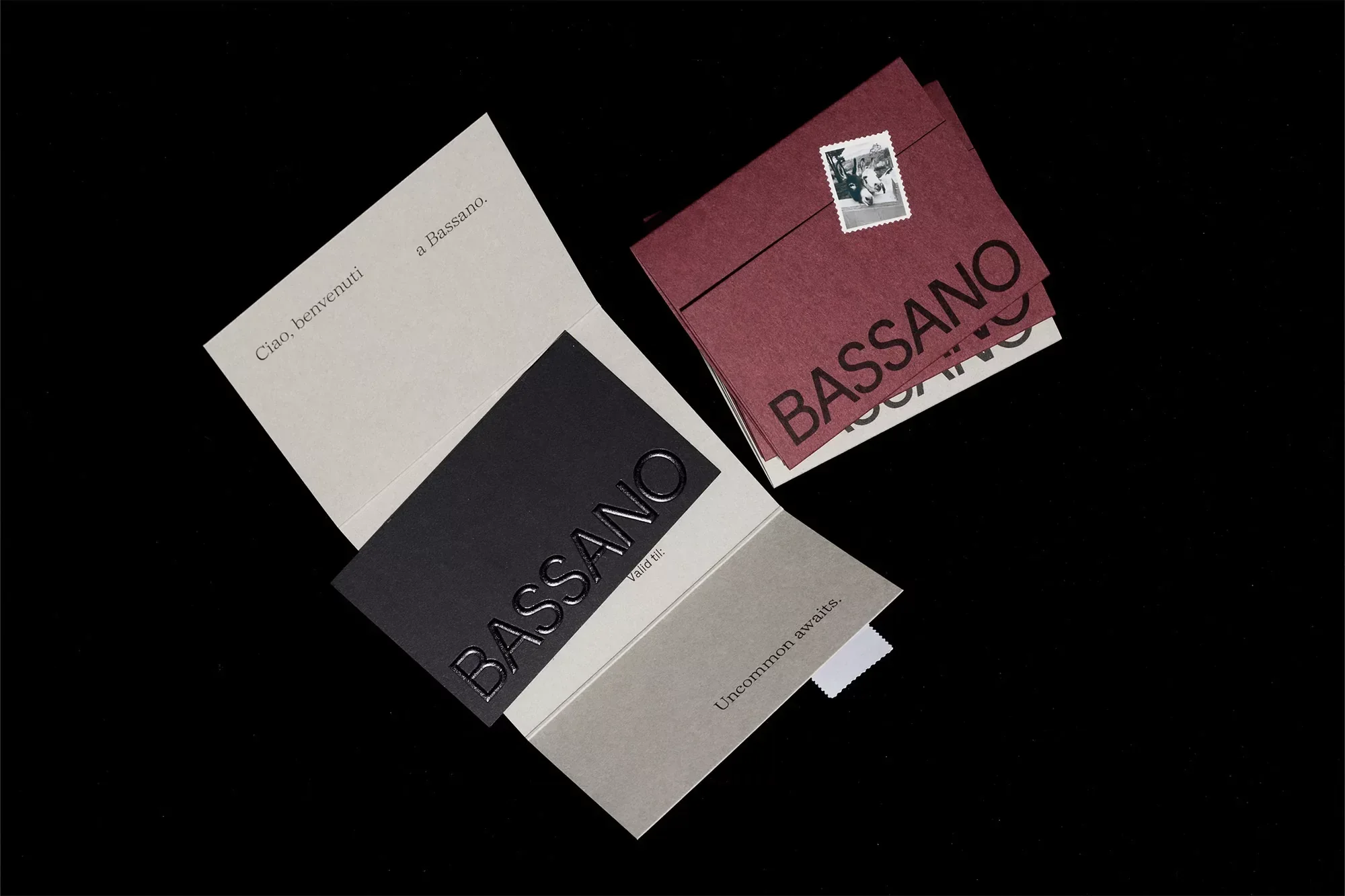 Overhead studio shot of an arrangement of gray, black, and maroon printed paper cards and envelopes with embossed text on a black backdrop.