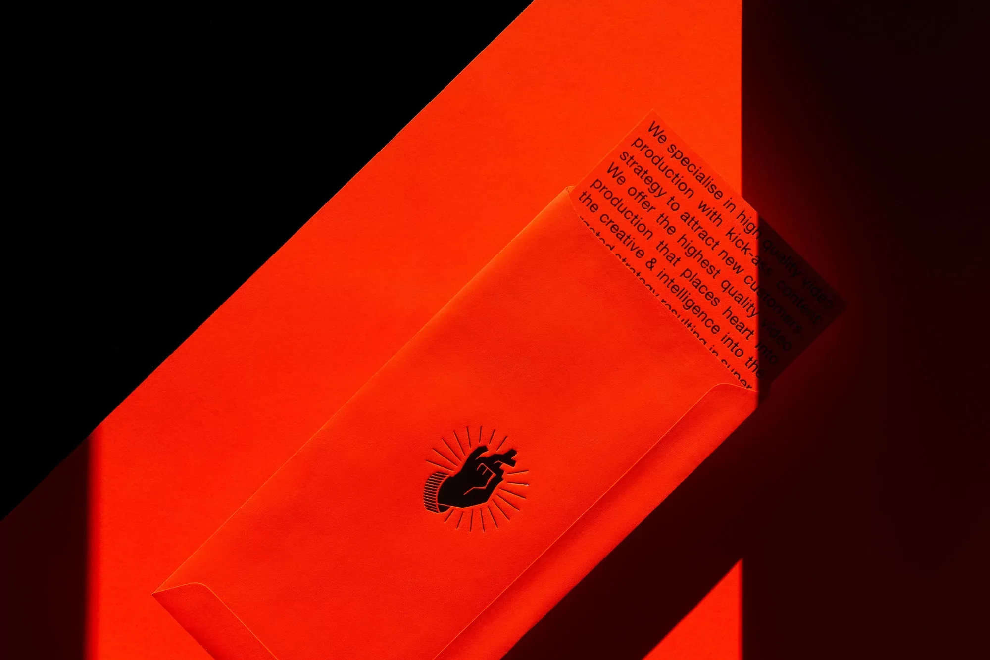 Close-up studio shot of a vibrant orange envelope with text and hand logo against a contrasting black background, showcasing brand design.