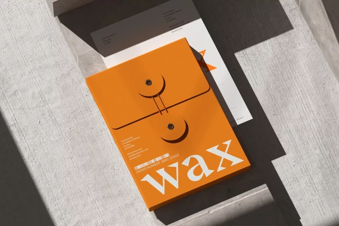 Eye-level shot of an orange stationery holder with the word "wax" in white, layered with a letter and envelope on concrete.