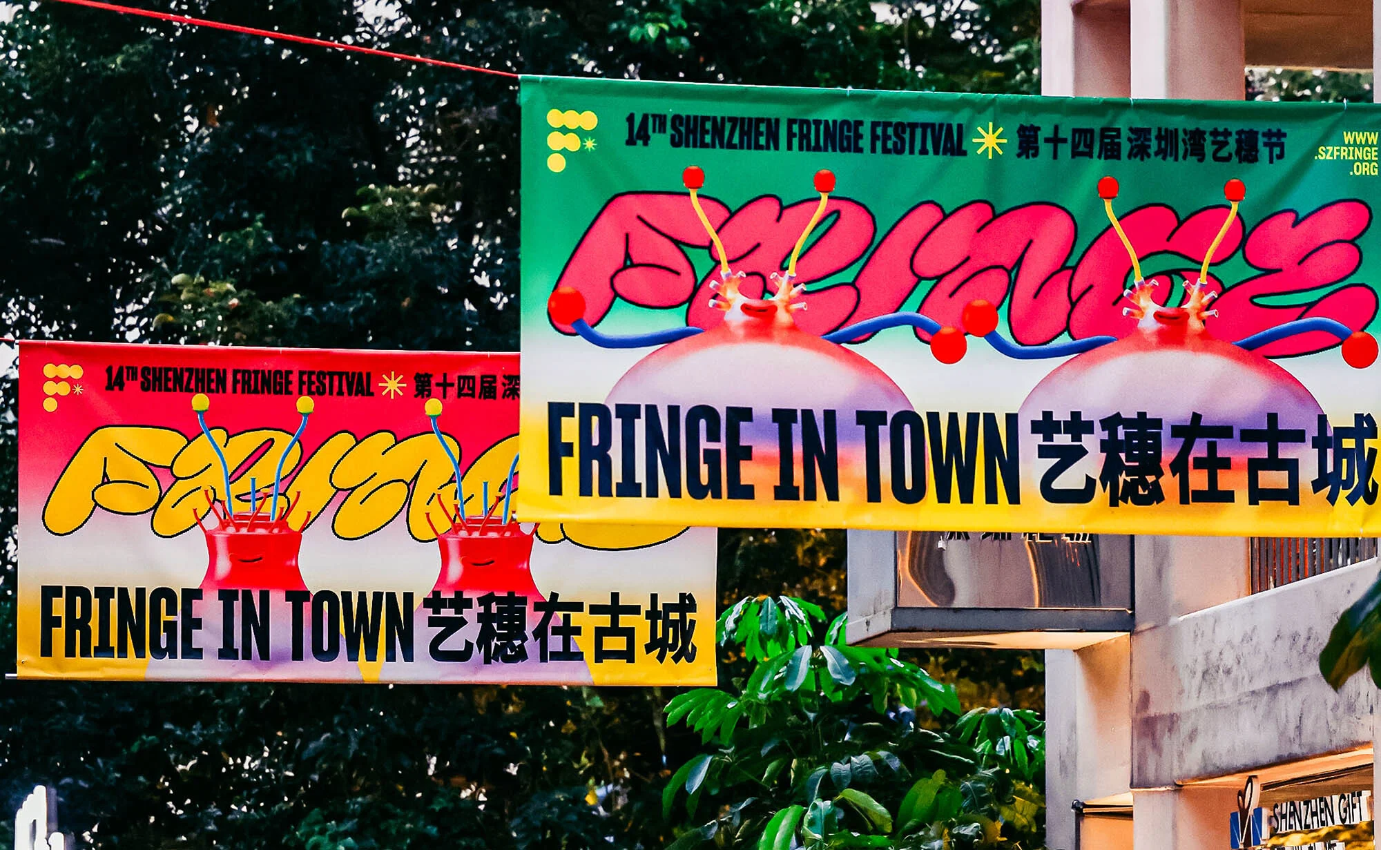 Two Shenzhen Fringe Festival banners hang outdoors, featuring colorful, cartoonish designs with event details in English and Chinese characters.