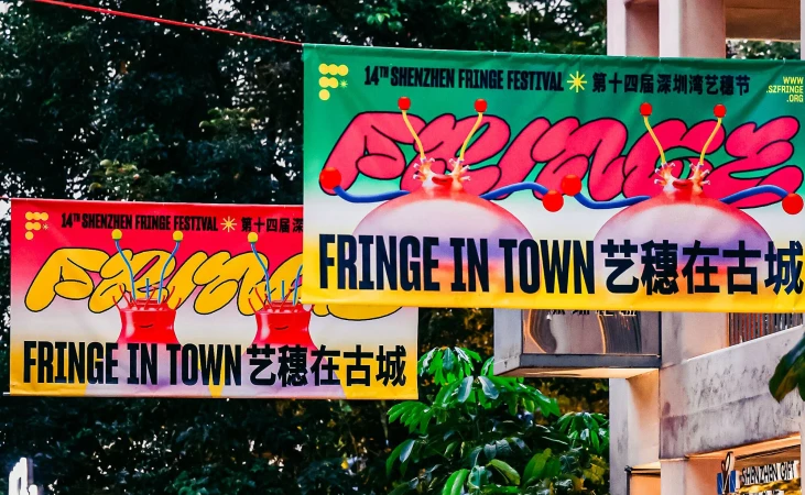 Two Shenzhen Fringe Festival banners hang outdoors, featuring colorful, cartoonish designs with event details in English and Chinese characters.