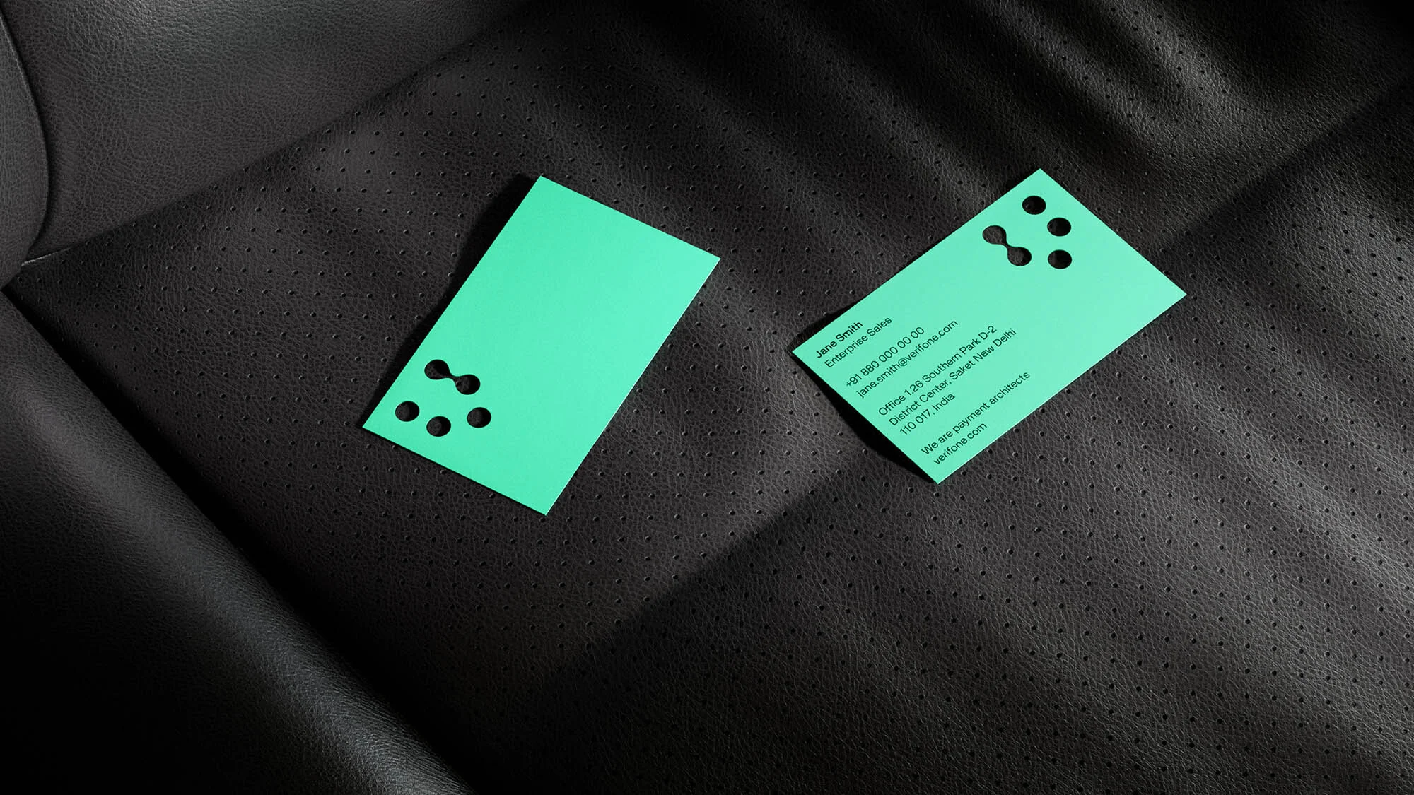 Two green business cards with unique cutout designs resting on a black leather surface, offering a clean and modern aesthetic.
