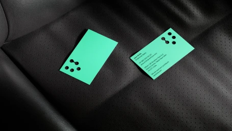 Two bright turquoise business cards with rounded cutouts resting on a perforated black leather surface.