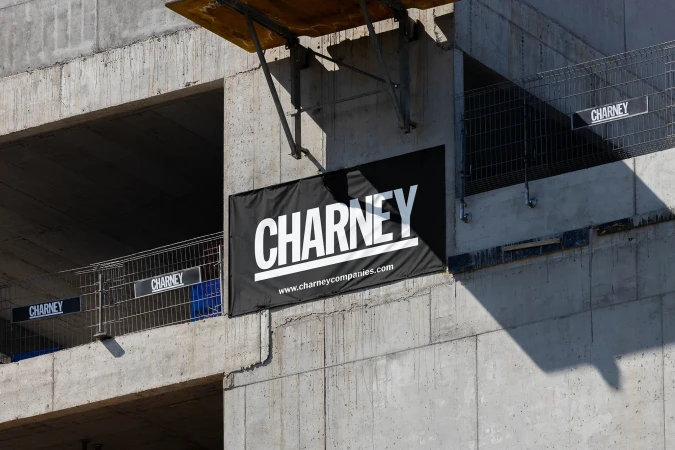 Construction site featuring a large black banner with the company name 'CHARNEY' and website address on a concrete structure.