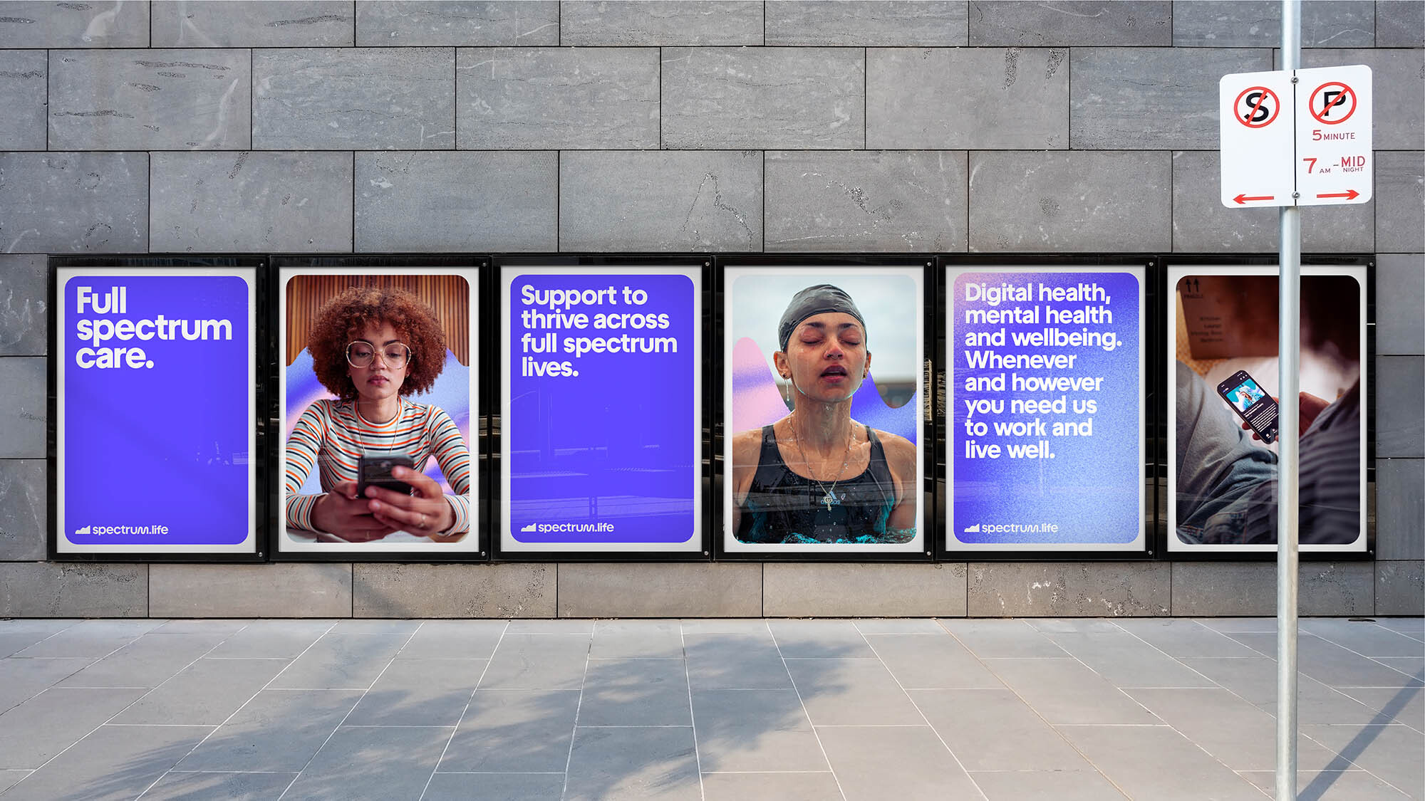 Urban setting displaying Spectrum Life advertisements on a gray brick wall with images and text promoting mental health and wellbeing.