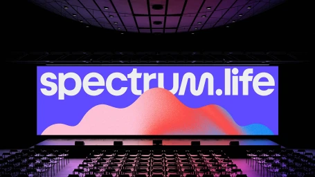 Wide view of an empty auditorium with rows of seats facing a large illuminated screen displaying the Spectrum Life brand identity.