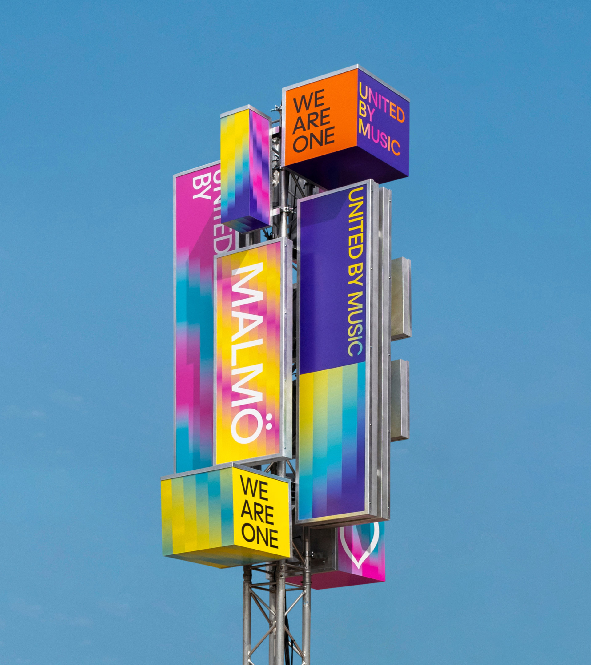 Metal tower features stacked signage with colorful blurred abstract designs, city name MALMÖ, against clear blue sky background outdoors.