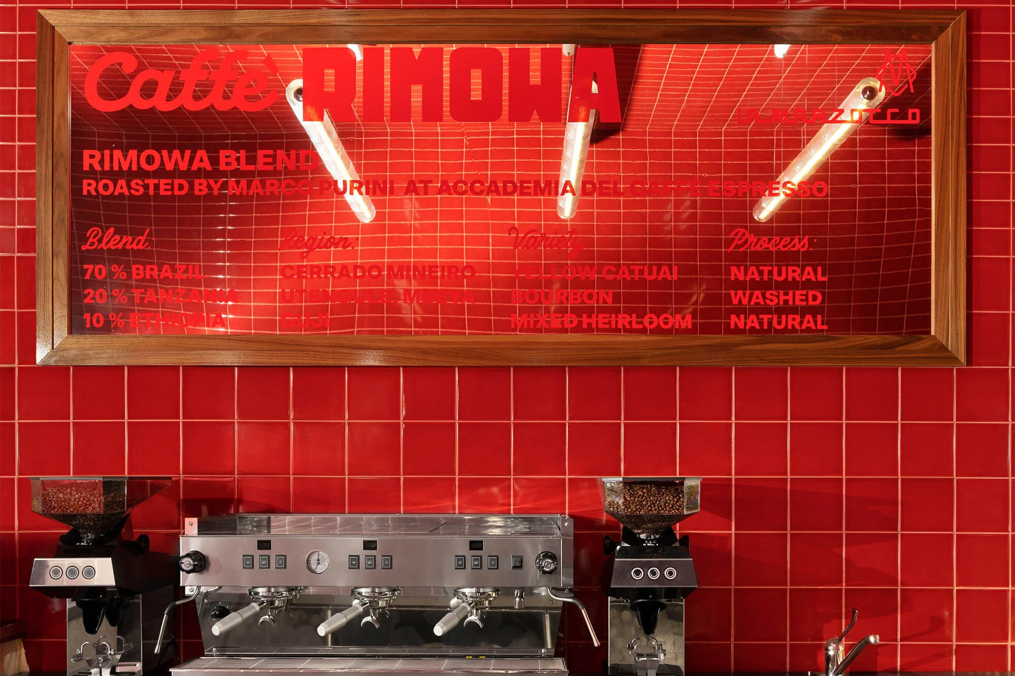 Commercial coffee shop scene features espresso machine with whole coffee beans, illuminated menu board, and red tile backsplash.