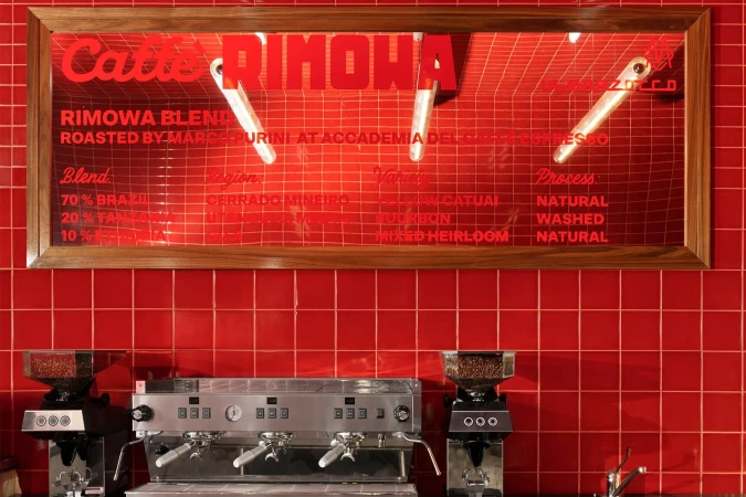 Commercial coffee shop scene features espresso machine with whole coffee beans, illuminated menu board, and red tile backsplash.
