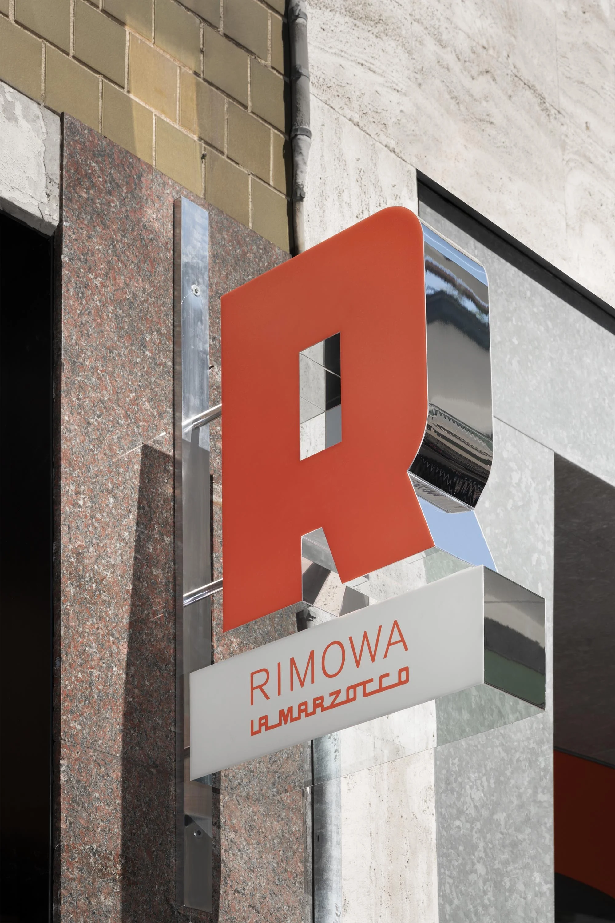 Outdoor sign for Rimowa and La Marzocco brands, featuring an orange R logo and metal framework against a building facade.
