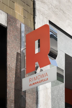 Outdoor sign for Rimowa and La Marzocco brands, featuring an orange R logo and metal framework against a building facade.