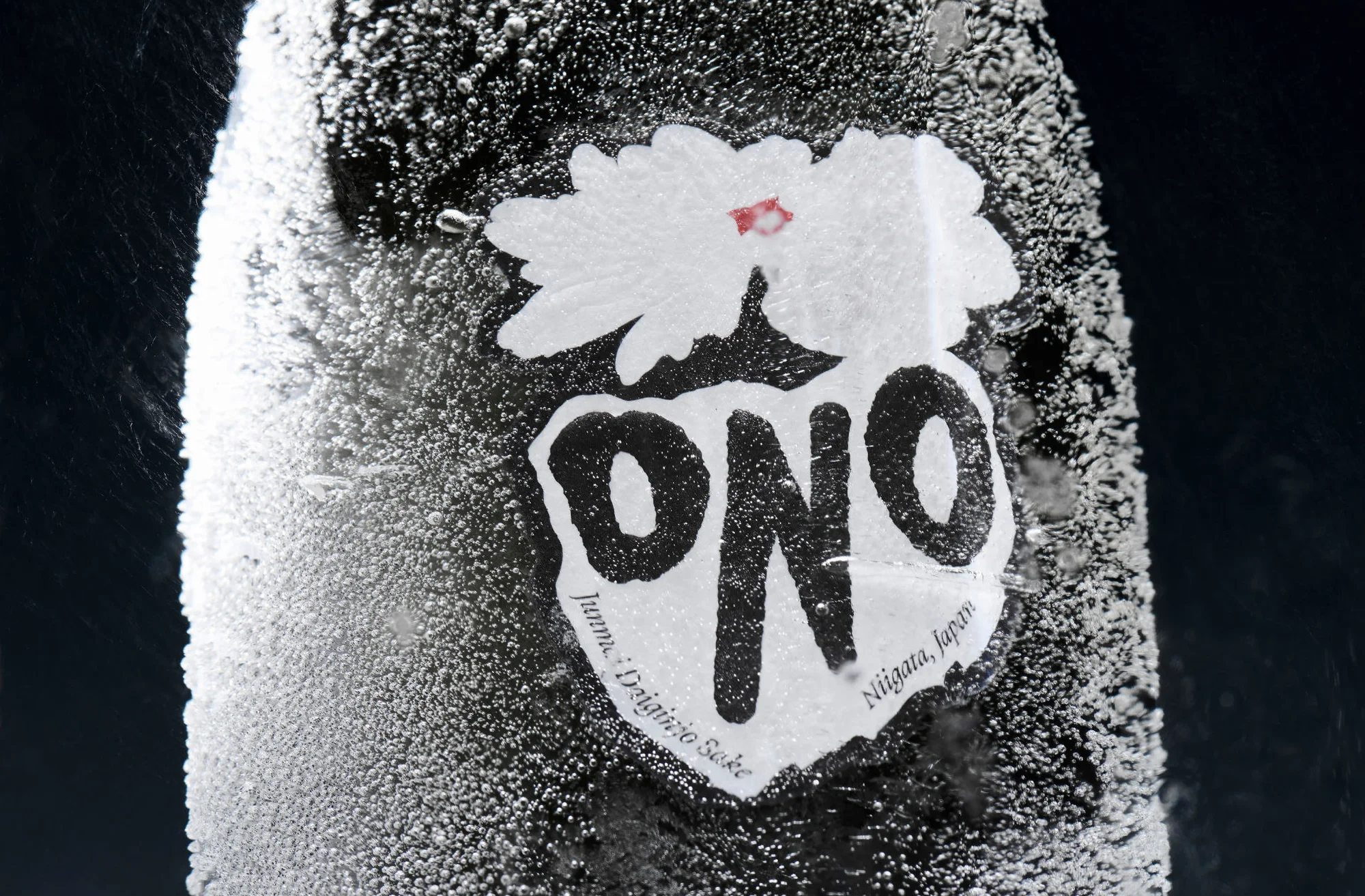 Close-up of a frosty sake bottle with a white label featuring a flower and the word "ONO," set against a dark, contrasting background.