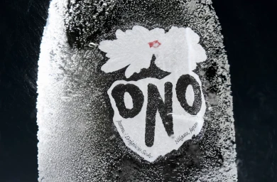 Close-up shot of a cold sake bottle covered in condensation droplets, featuring the bold white and black label for Sake Ono.