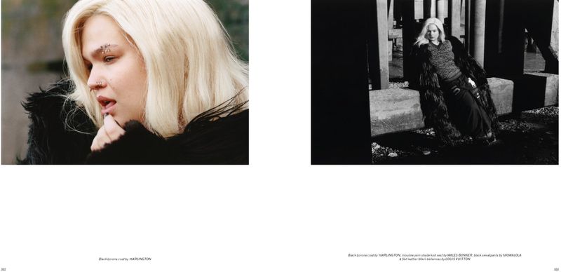Editorial fashion shot of a model with platinum blonde hair wearing a black furry coat in a concrete and stone outdoor environment.