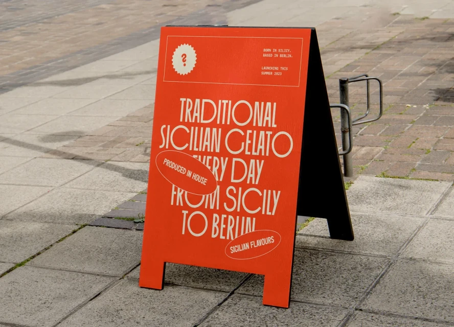 Sidewalk advertisement sign for Sicilian gelato in Berlin, featuring text about traditional gelato and being produced in-house.