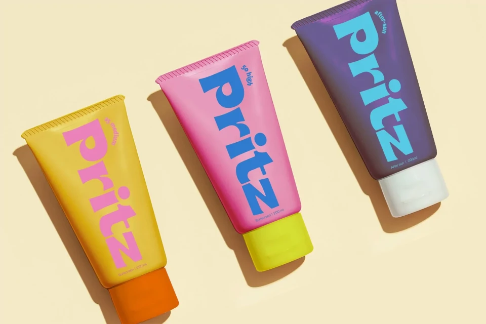 Three tubes of brightly coloured Pritz sunscreen with orange, yellow, blue and pink colour schemes against a light yellow backdrop.