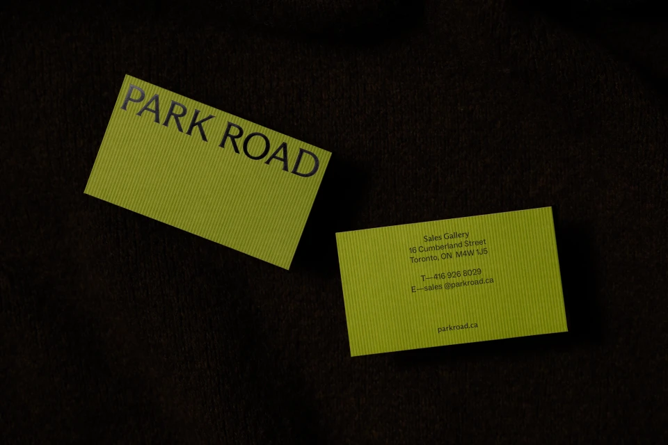 Two light green business cards with black text are displayed against a textured dark brown background, one overlapping slightly.