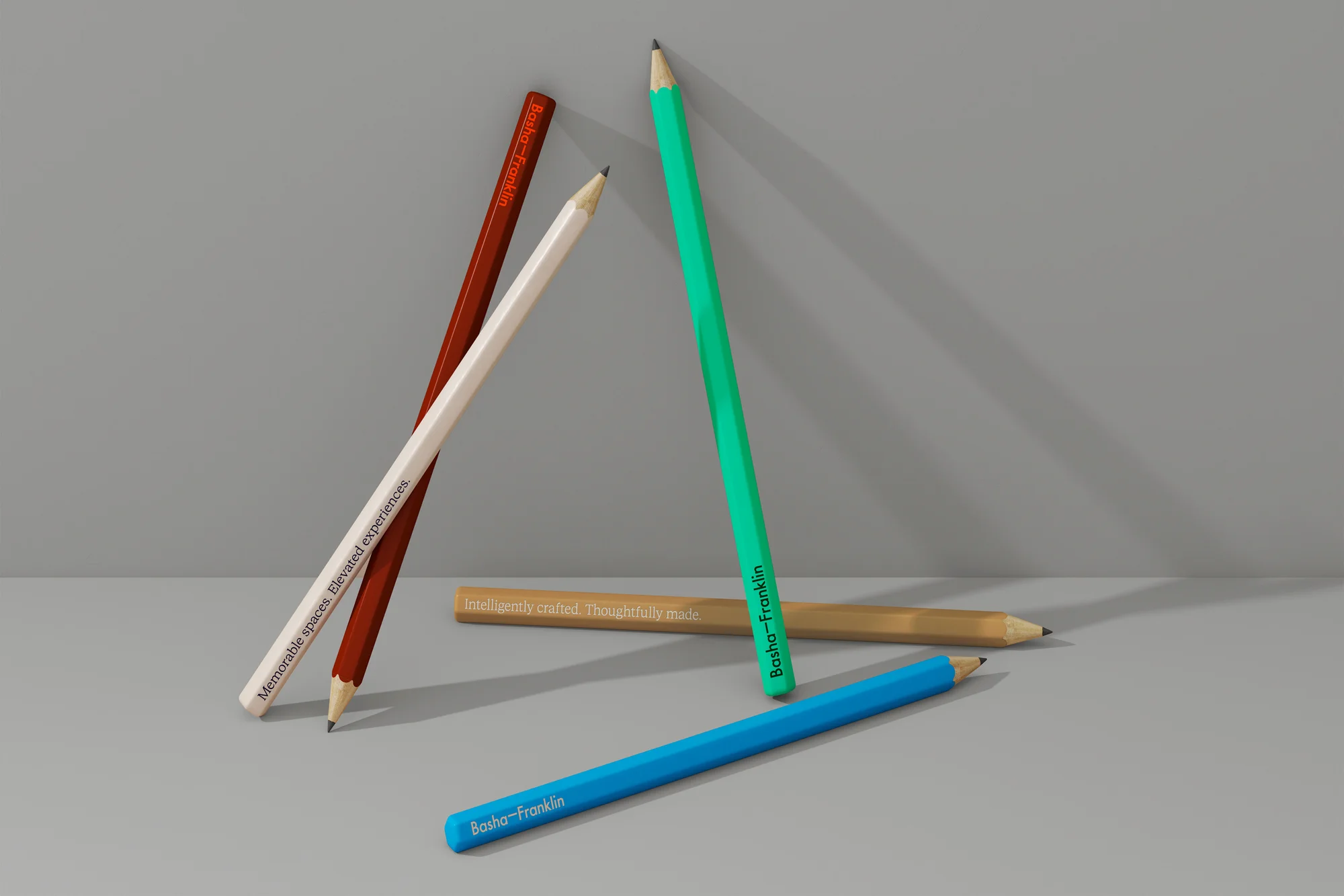 Still life of colorful pencils angled against a grey wall. The pencils have printed brand names on them in black. 