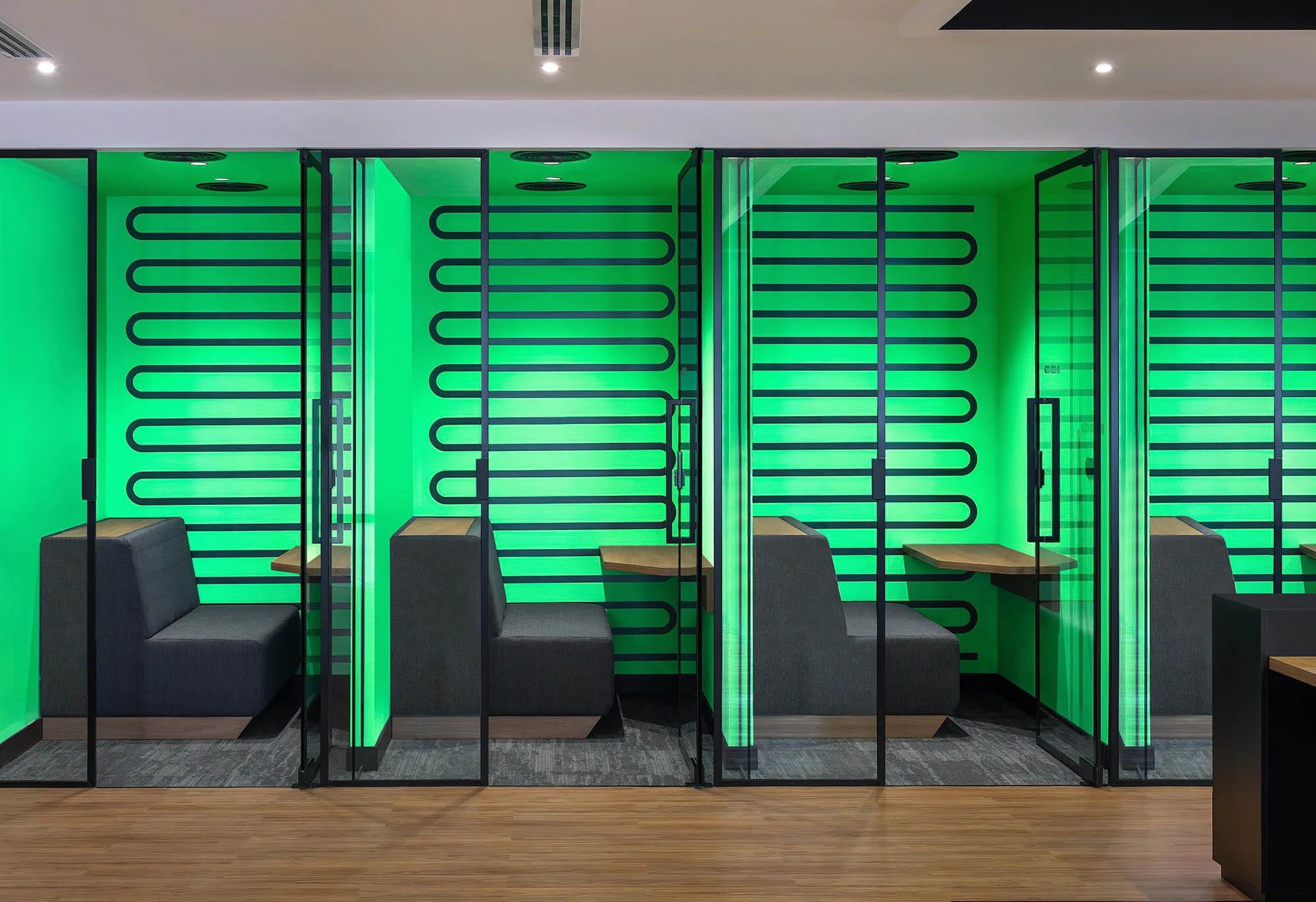 Modern office interior featuring soundproof booths with gray sofas, wood tables, bright green walls, and black metal frames. Interior design.