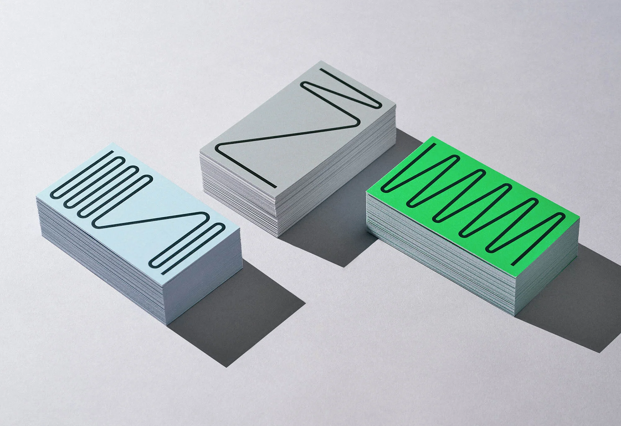 Three stacks of colorful business cards with graphic black line patterns displayed on a white surface with shadows, creating a minimalist design.