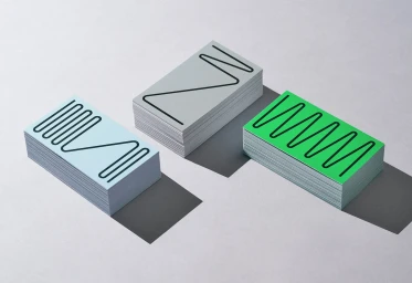 Three stacks of business cards in blue, grey, and green with black line art patterns on a grey surface.