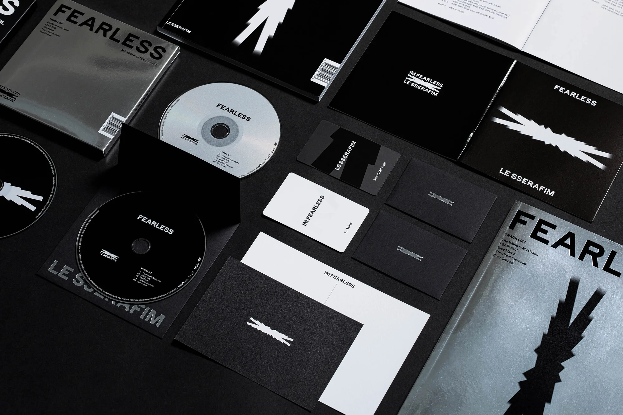 Still life product shot of LE SSERAFIM's album 'FEARLESS' featuring CDs, cards, and cover art on a black background.