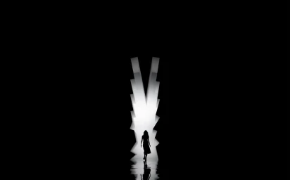 Silhouette of a person walking towards a bright V-shaped portal in a dark room with a reflective floor.