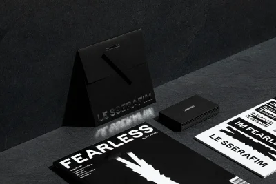 LE SSERAFIM brand identity collateral including black packaging, business cards, and a Fearless magazine laid out on dark slate stone