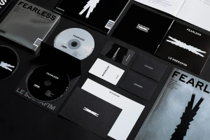 Flat lay arrangement of LE SSERAFIM FEARLESS brand identity items including compact discs, lyric booklets, and photo cards on a dark surface.