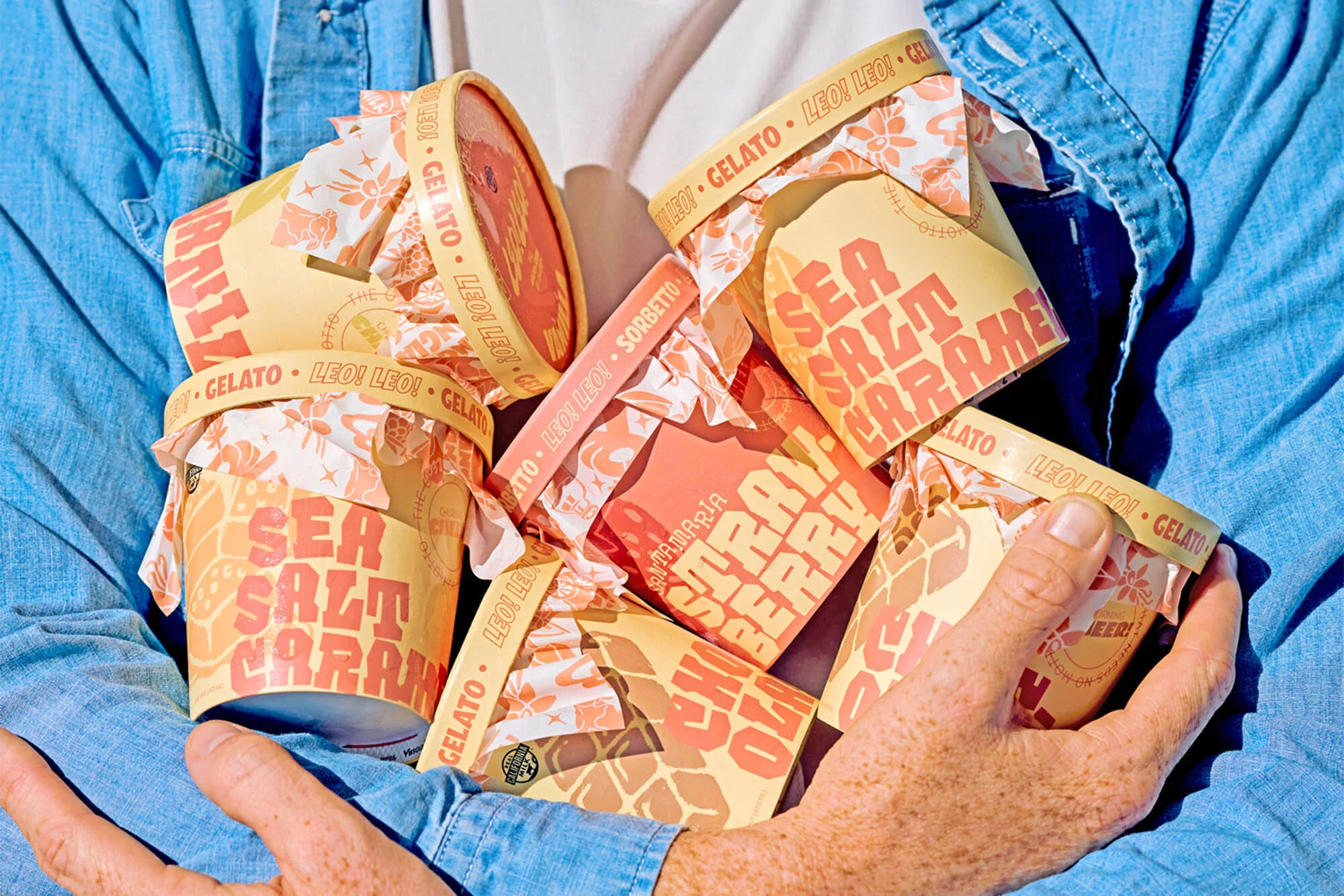 Person holds multiple paper gelato and sorbetto containers in a casual, well-lit food and beverage product shot featuring vibrant colors.