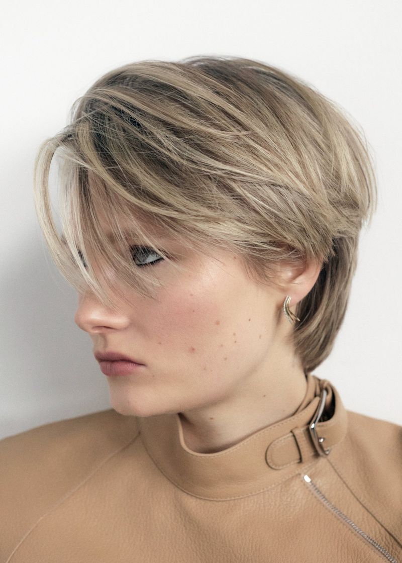 Blonde woman with layered pixie hairstyle wearing a beige leather top in a studio portrait. Hair, fashion, and beauty concept.