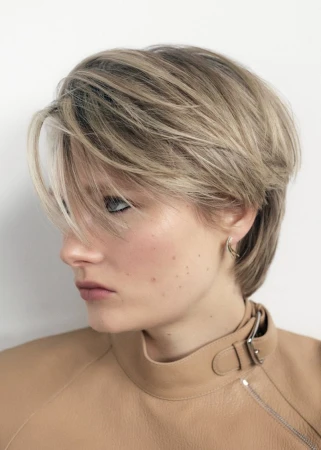 Blonde woman with layered pixie hairstyle wearing a beige leather top in a studio portrait. Hair, fashion, and beauty concept.