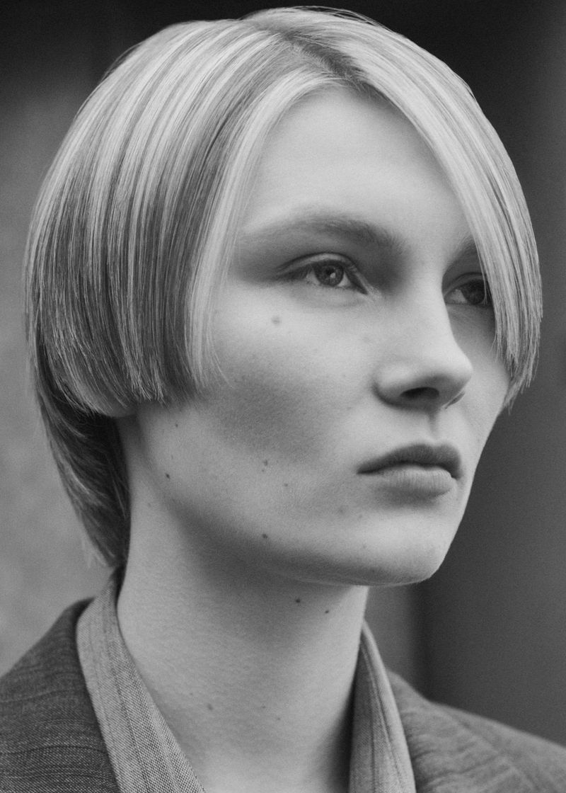 Monochrome portrait of a young adult female with blonde hair, looking off-camera while wearing a grey blazer.