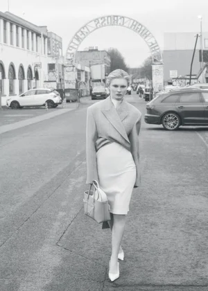 Model walking down a paved street carrying a handbag wearing a structured blazer and dress