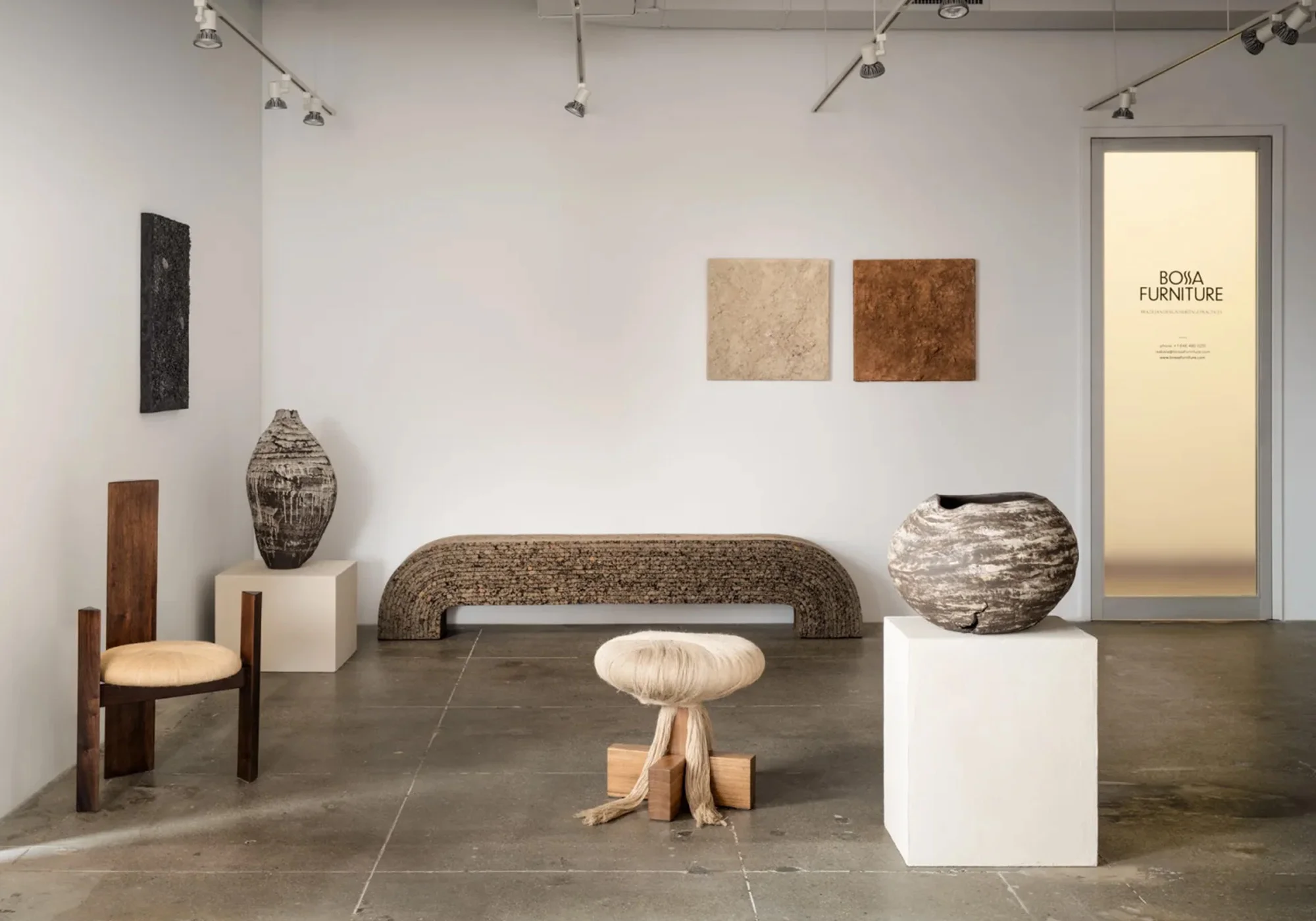 Interior of a design studio showcasing unique furniture pieces, including a wooden chair, bench, vases, and artistic wall decor in a minimalist space.