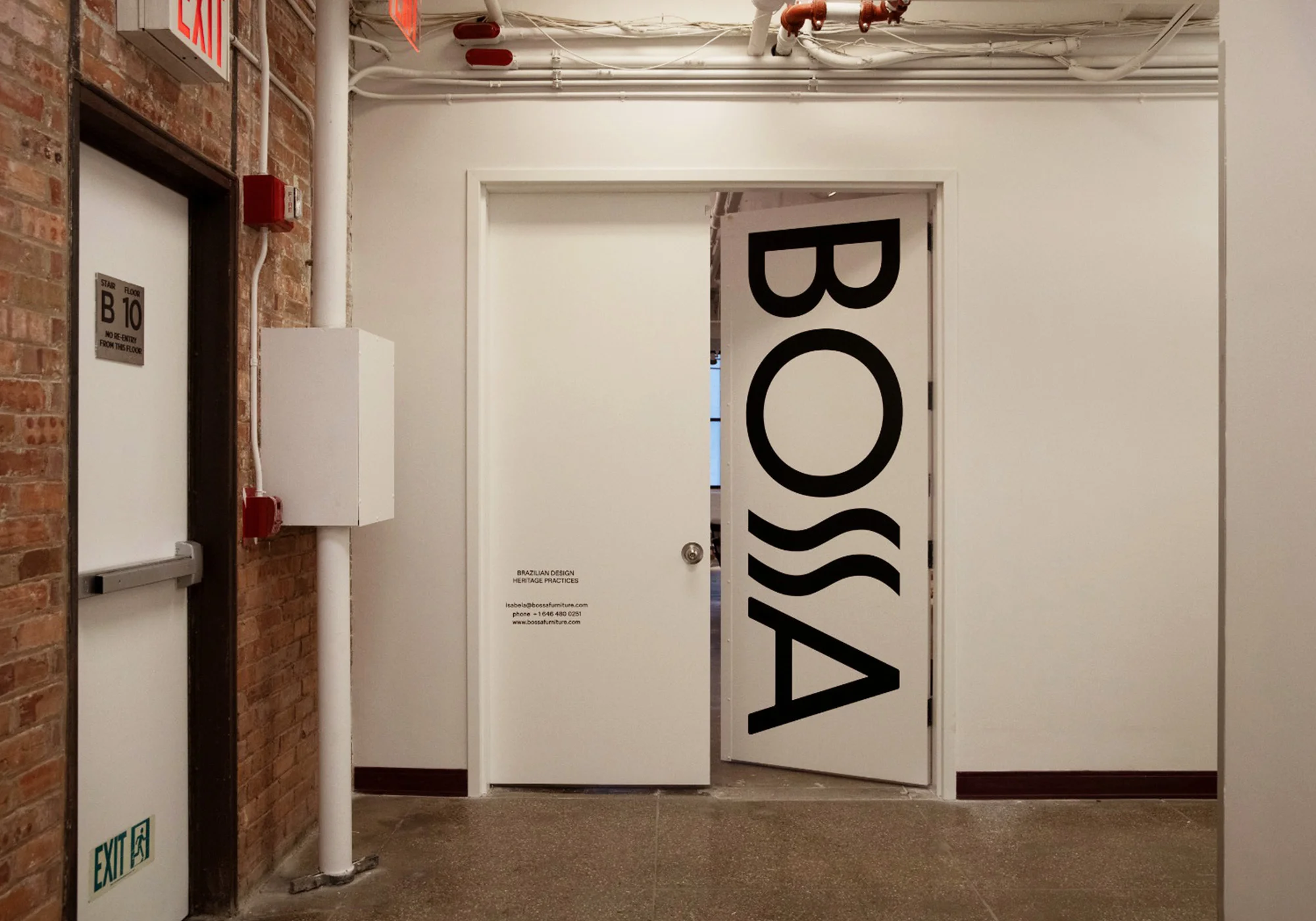 White door with 'Bossa' text in modern office interior featuring brick wall and concrete floor. Industrial building hallway.