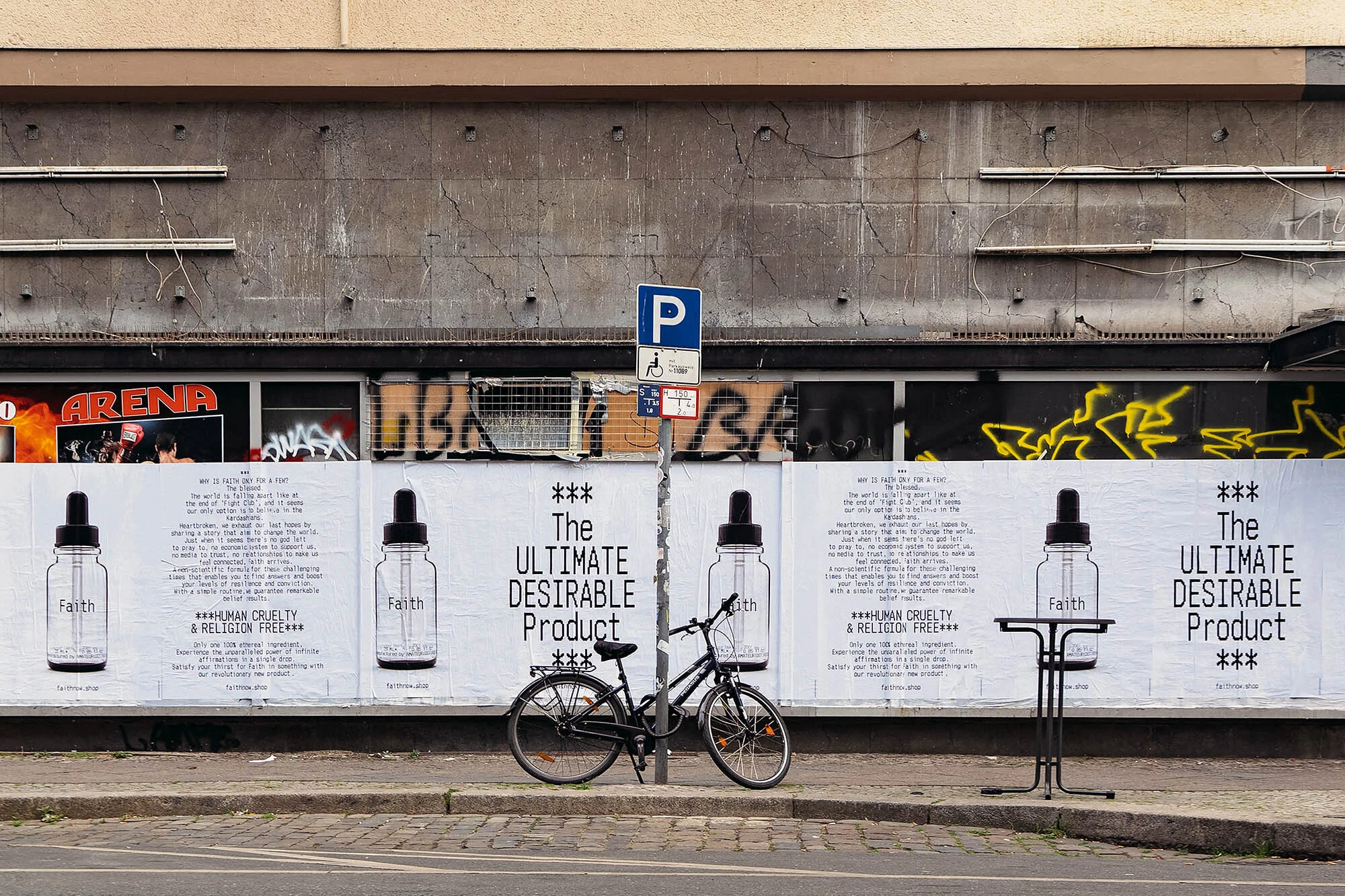 Urban scene with a bicycle parked in front of posters advertising a product called Faith, emphasizing human cruelty and religion-free values.
