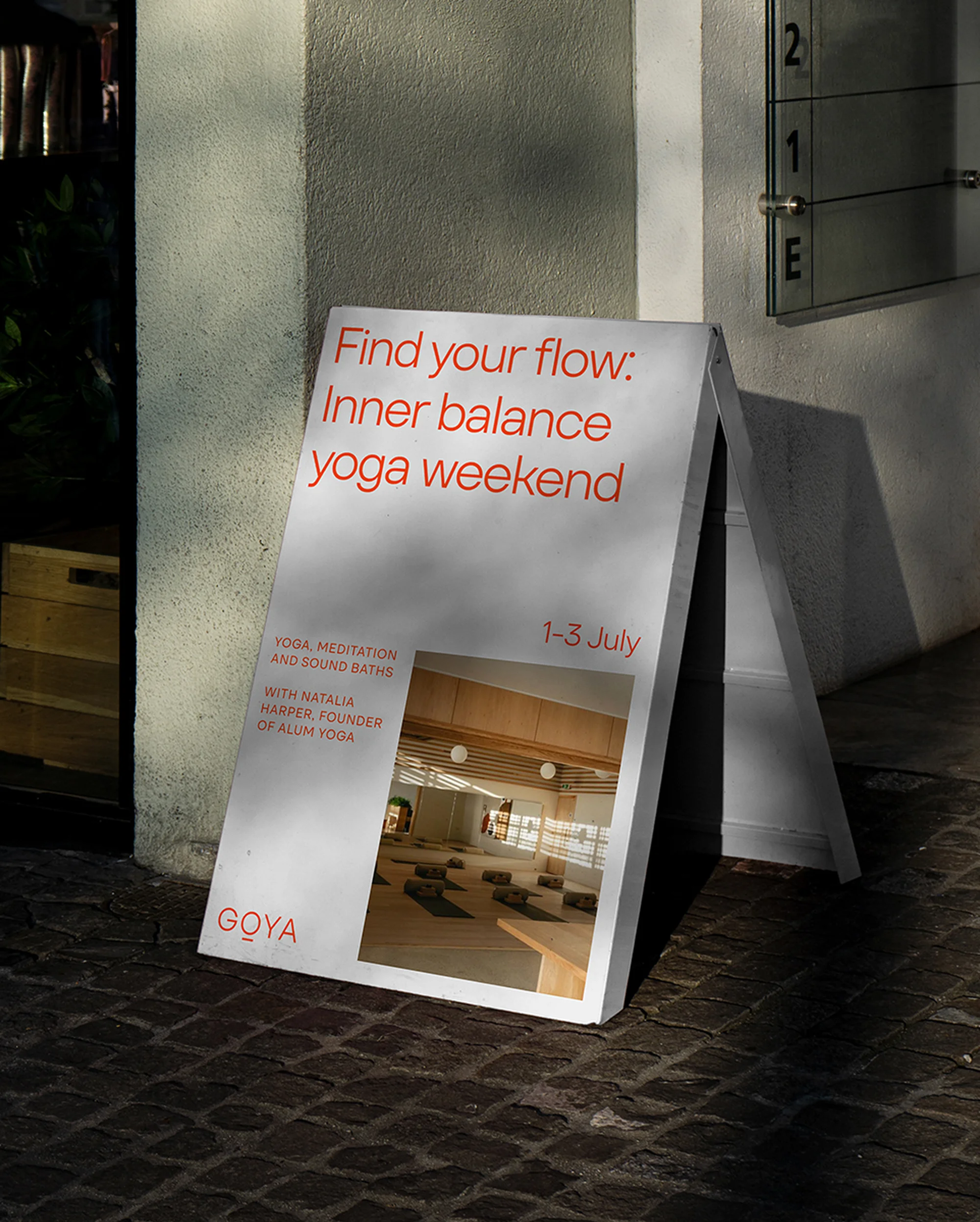 Sidewalk advertising poster for 'Inner Balance Yoga Weekend' features event dates, brand name 'Goya,' and tranquil yoga studio interior.