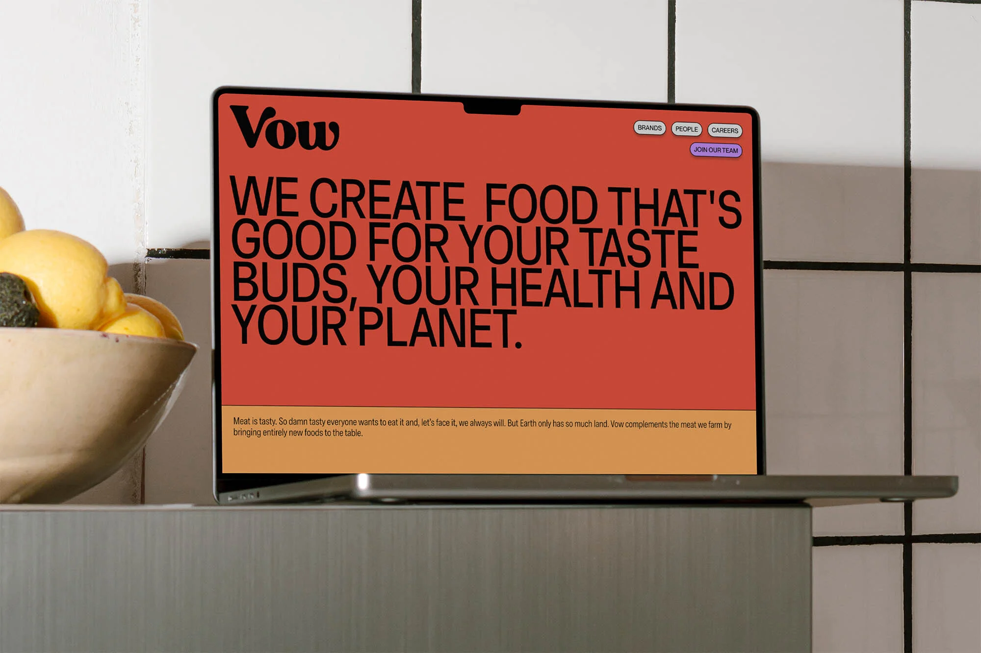 Laptop displays Vow website with 'We Create Food That's Good For Your Taste Buds, Your Health and Your Planet' on terracotta background.