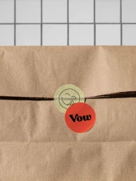 Brown paper package tied with dark string featuring a red sticker with Vow branding and a yellow sticker with a smiling face illustration.