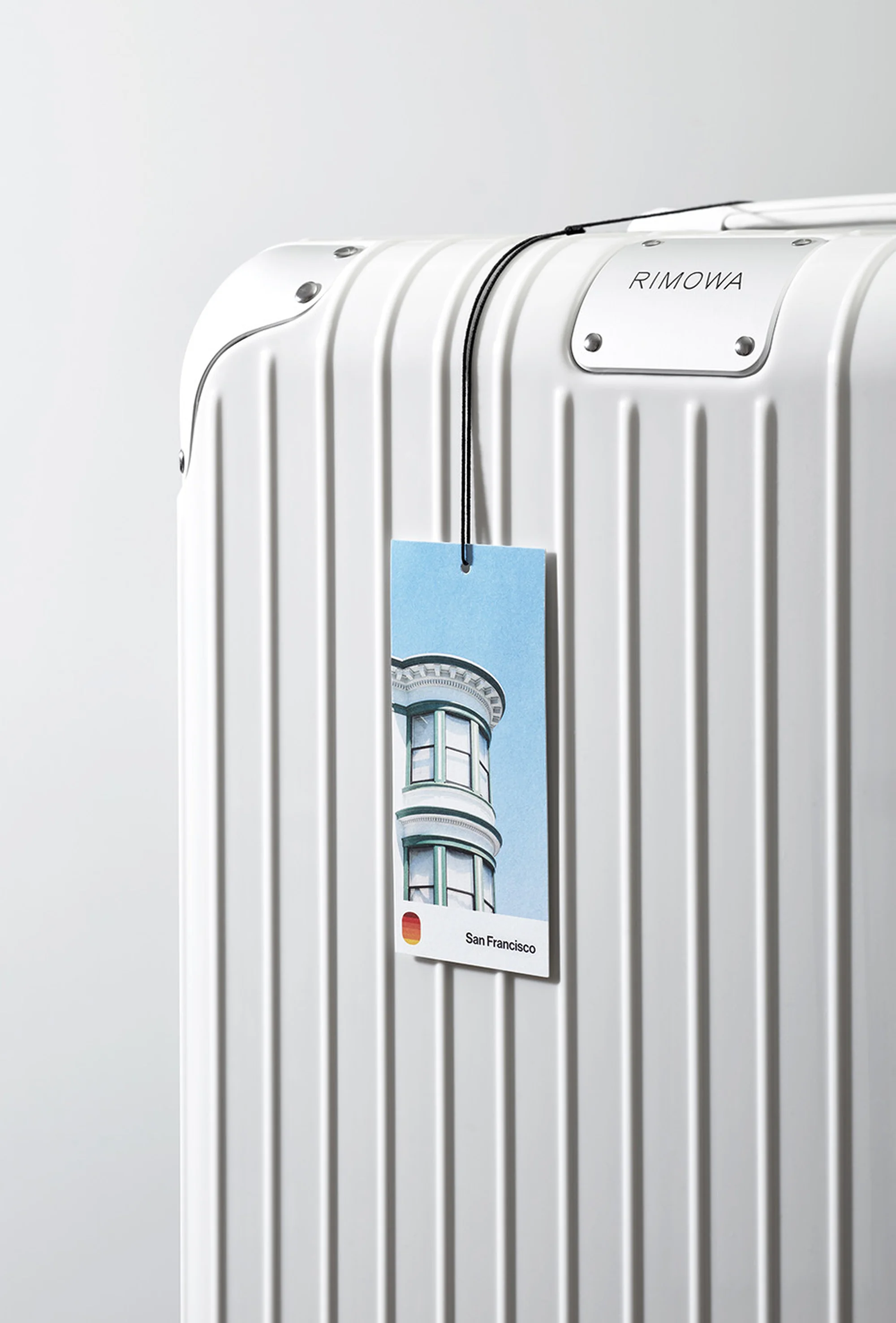 White Rimowa suitcase with a San Francisco themed luggage tag, showcasing urban travel and sleek design against a clean background.