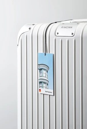 White Rimowa suitcase with a San Francisco themed luggage tag, showcasing urban travel and sleek design against a clean background.