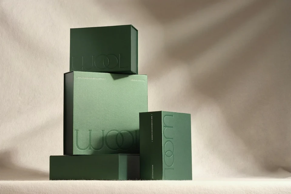 Stacked green boxes with embossed text on a beige surface with shadow, creating a minimalist and elegant presentation.